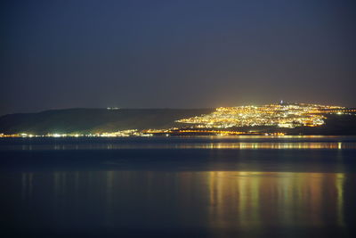 Illuminated city by sea against clear sky at night