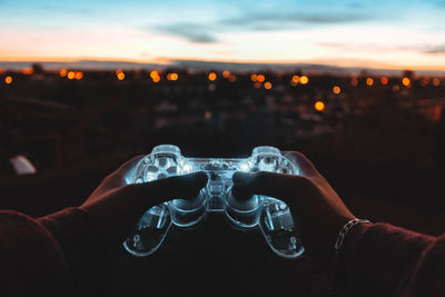 Close-up of hand against illuminated lights during sunset