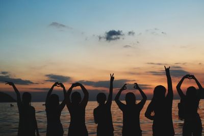 Silhouette people gesturing at beach against sky during sunset