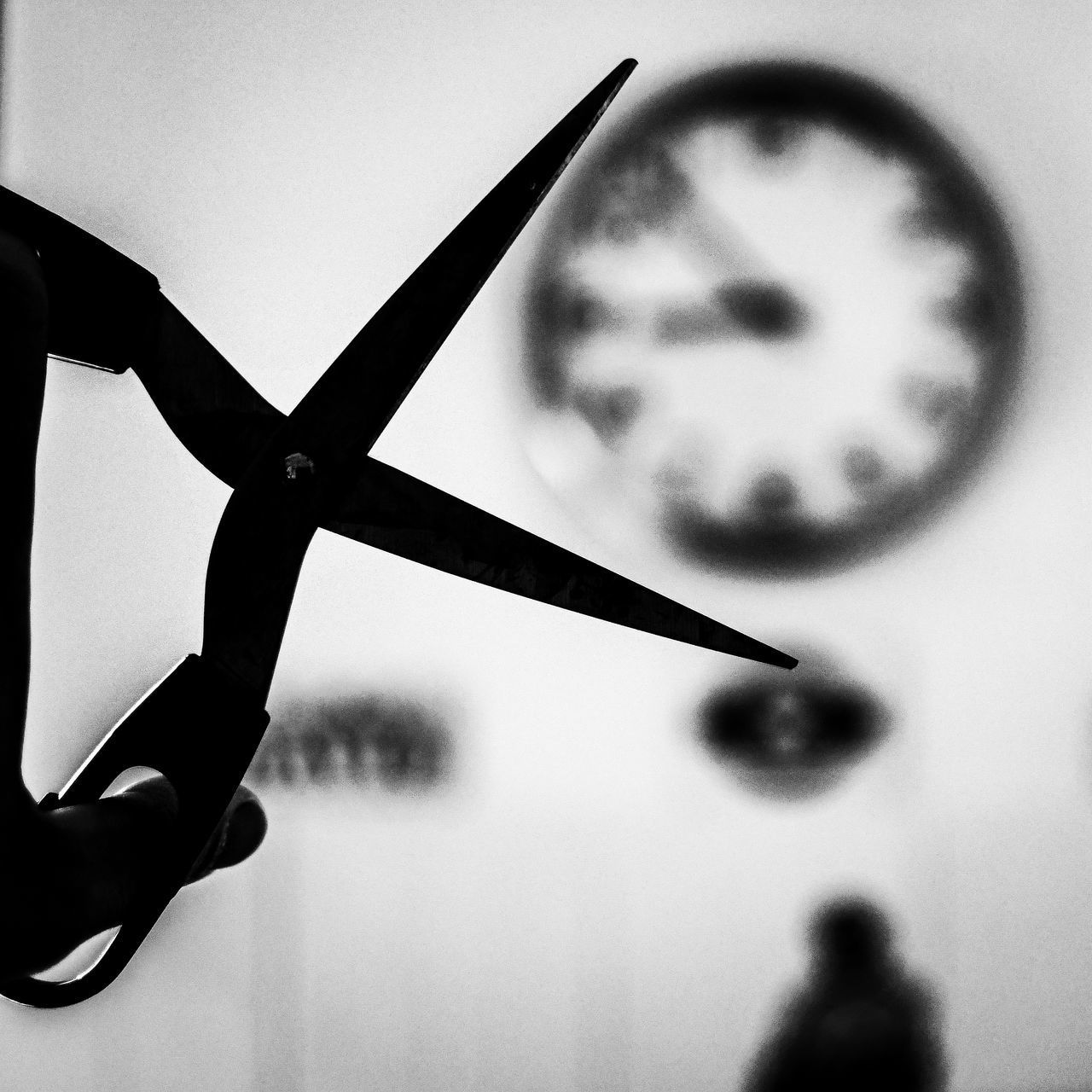 CLOSE-UP OF HAND HOLDING SILHOUETTE CLOCK AGAINST METAL