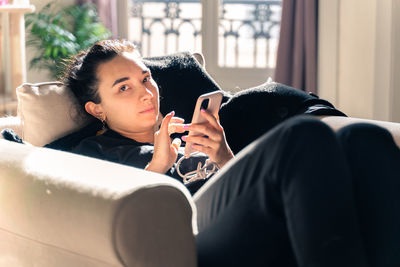 Portrait of young woman using mobile phone sitting on sofa