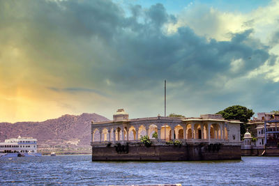 Buildings at waterfront against cloudy sky in udaipur rajasthan india