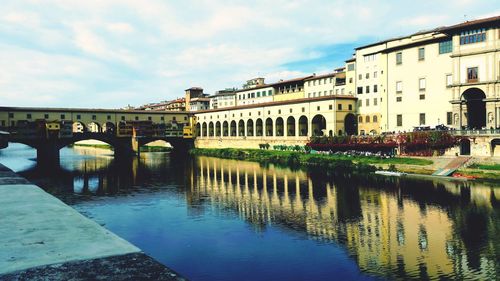 Arch bridge over river by buildings against sky