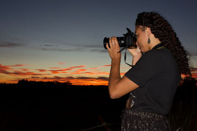 Young woman with a camera, shooting the sunrise, colorful sky.