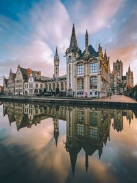 Reflection of historic buildings in canal against cloudy sky