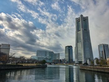 Yokohama landmark tower and buildings by canal against sky