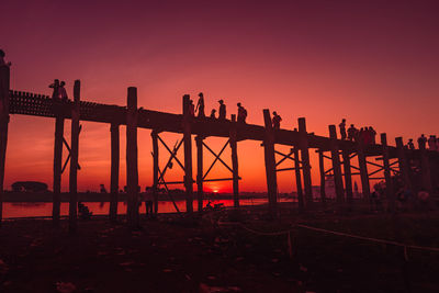 Silhouette bridge over sea against sky during sunset