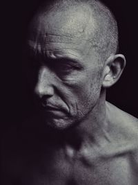 Close-up portrait of shirtless man against black background