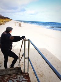 Man standing on railing by sea against sky