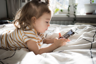 Boy using mobile phone while lying on bed at home