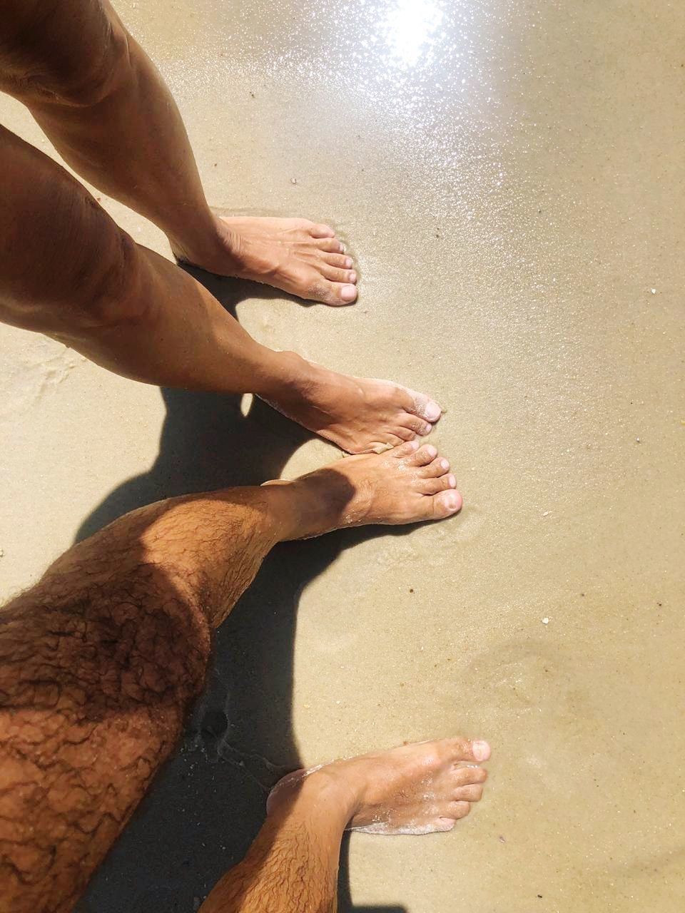 human body part, real people, human leg, body part, sand, beach, people, land, water, low section, barefoot, men, two people, sunlight, high angle view, human foot, nature, lifestyles, sea, hand, outdoors