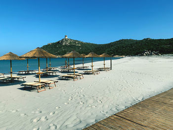 Deck chairs on beach against clear blue sky