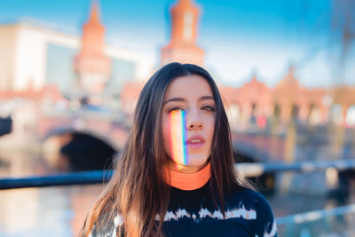 Sunlight falling on young woman standing against bridge over river in city