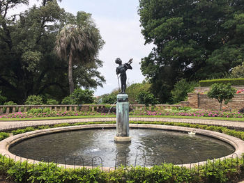 Statue by fountain in park against sky