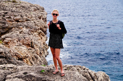 Full length of young woman standing on rock by sea