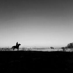 Silhouette man riding horse on field against clear sky