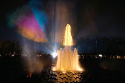 Illuminated fountain in city against sky at night