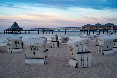 Hooded chairs on beach against sky during sunset