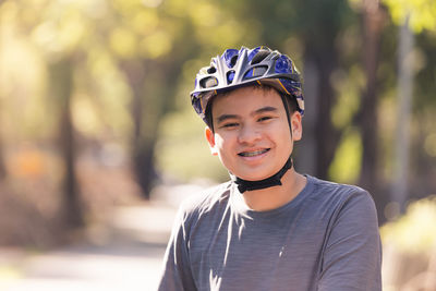 Portrait of smiling teenage boy wearing cycling helmet while standing outdoors