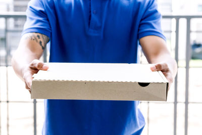 Midsection of salesman with cardboard box standing at gate way