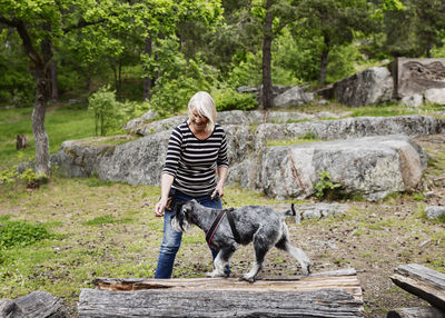 Playful senior woman enjoying with dog walking on log at field