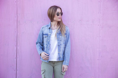 Young woman standing against pink wall