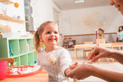 Girl looking at teacher while eating food at preschool