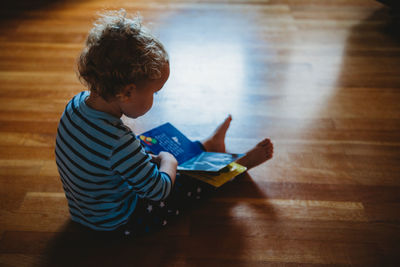 Rear view of boy sitting on hardwood floor at home