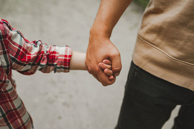 Hands of father and child. father holds tightly small hand of cute child in checkered red shirt