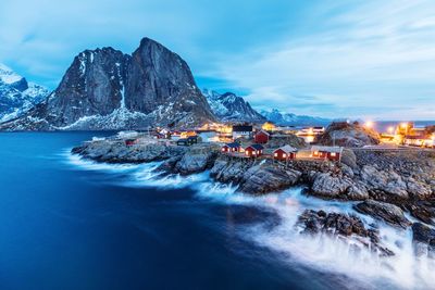 Illuminated mountain by sea against sky at dusk