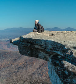 Man sitting on rock against blue sky