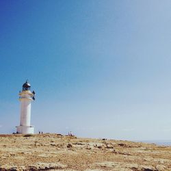 Lighthouse on landscape against clear blue sky