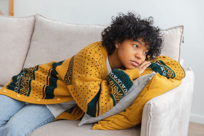 Young woman using phone while sitting on sofa at home