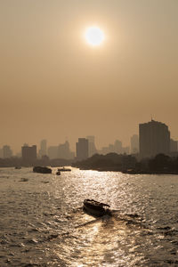 Sea by cityscape against clear sky during sunset