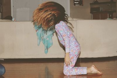 Side view of girl tossing hair while kneeling on hardwood floor at home