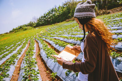 Woman wearing knit hat holding book while standing on field