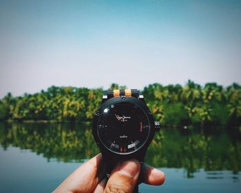 Person holding sunglasses against lake