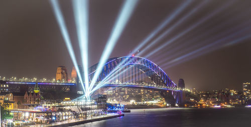 Illuminated bridge over river in city at night