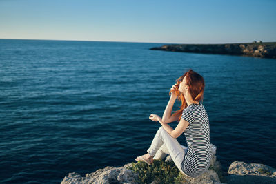 Woman sitting on rock by sea against sky