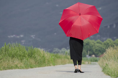 Rear view of mature woman holding umbrella while standing on road against mountain