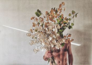 Shirtless man holding plant parts against wall