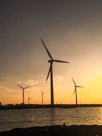 Silhouette cranes by sea against sky during sunset