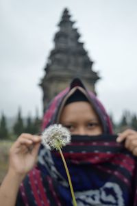 Portrait of woman holding pink flowering plant against sky