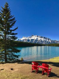 Empty red adirondack chairs at lakeshore against mt rundle during winter