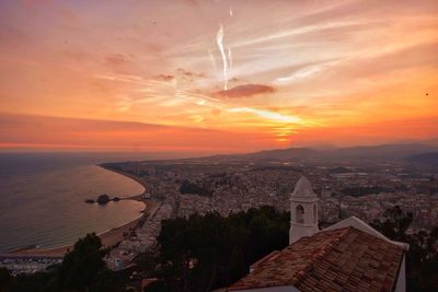 Aerial view of cityscape and sea against cloudy sky at sunset