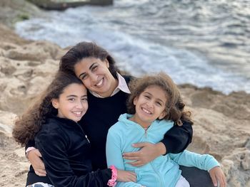 Portrait of mother with two young girls daughters sitting near the beach sea