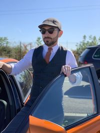 Man wearing sunglasses standing by car against sky