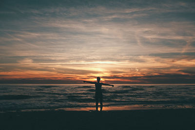 Silhouette man standing by sea against sky during sunset