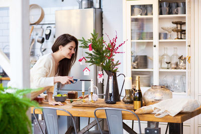 Smiling young woman igniting candle on table at home