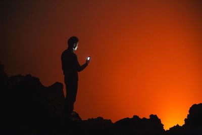 Silhouette man using mobile phone while standing on rocks during sunset